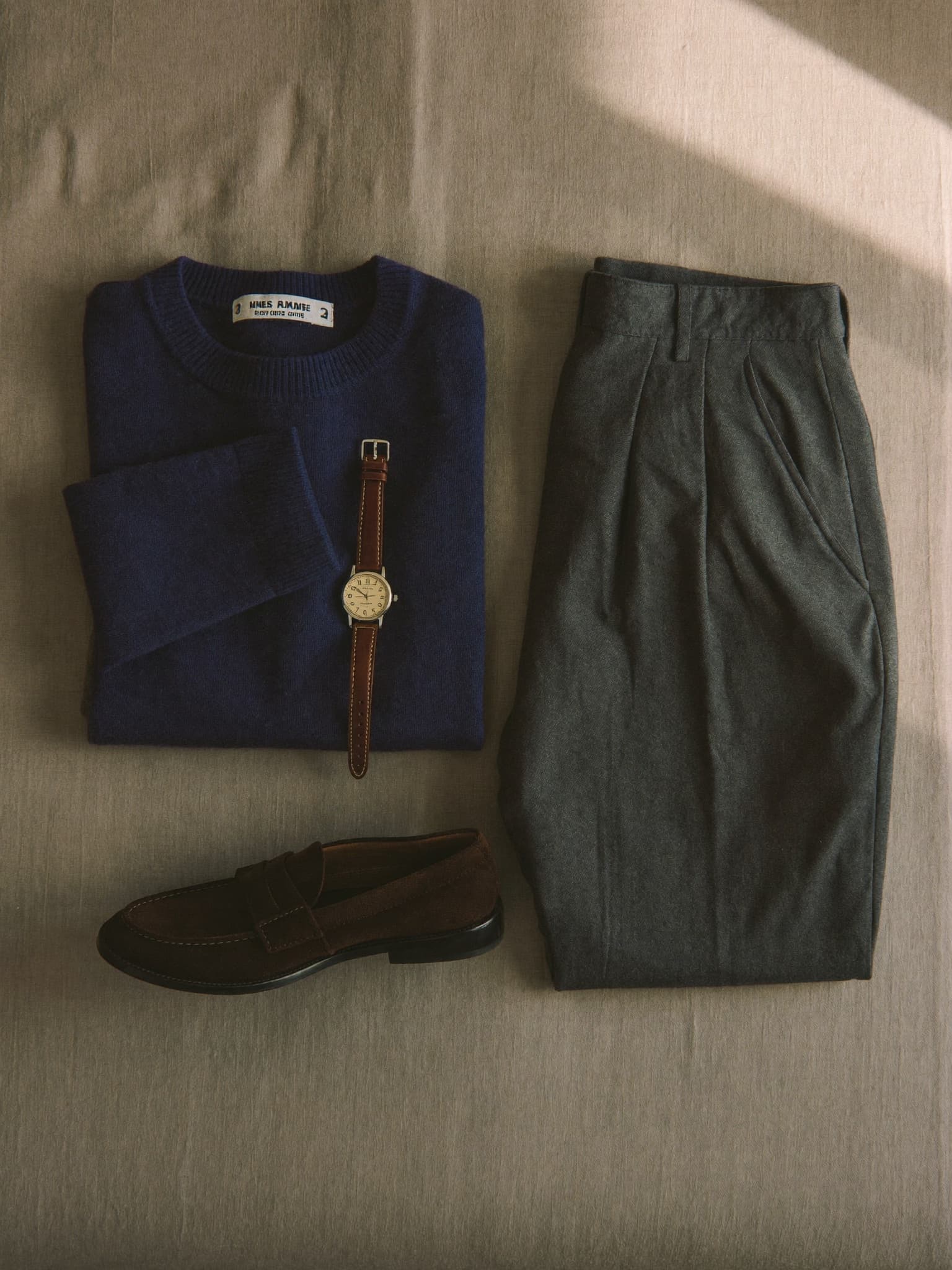 Flatlay der Smart-Casual-Formel: navy Strick, graue Wollhose, Wildleder-Loafer und Uhr
