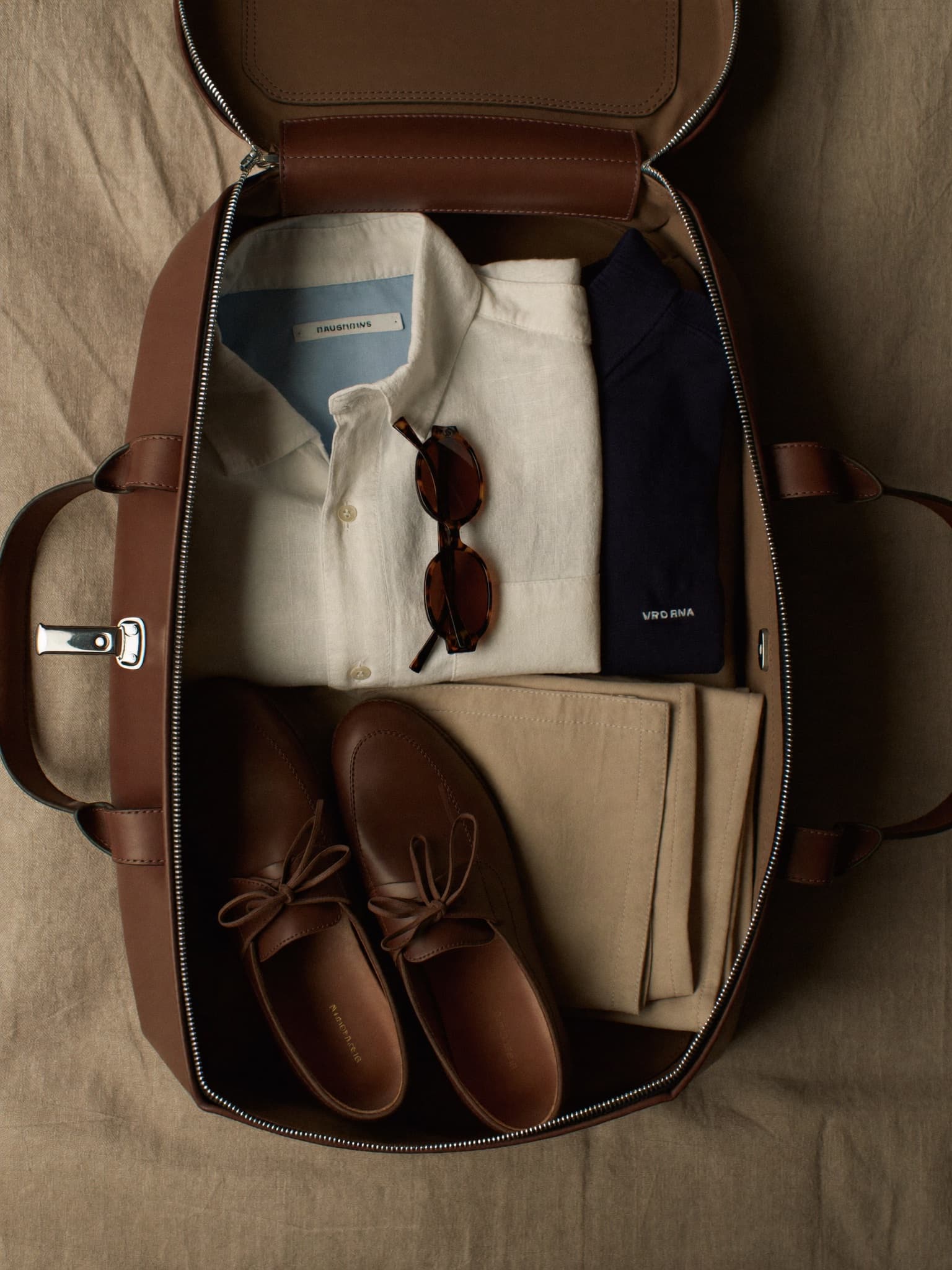 Gepackter Lederweekender mit Hemden, Chino, Loafern und Sonnenbrille von oben